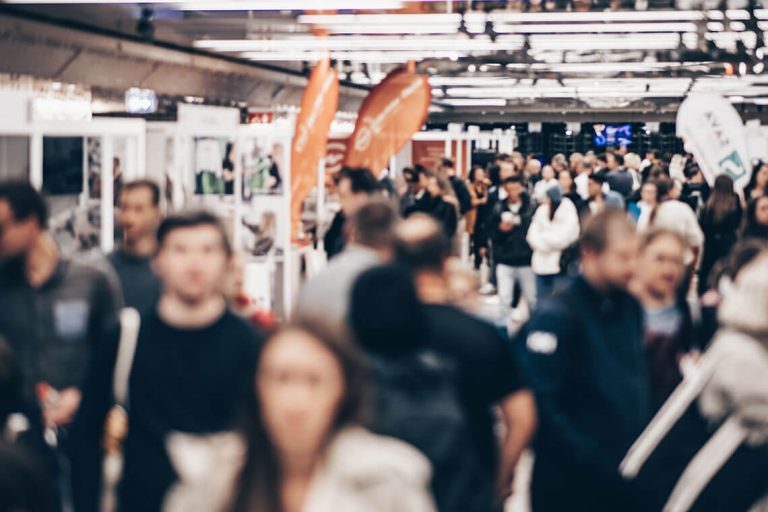 Pasillo de una feria lleno de visitantes entre los stands de los expositores